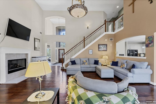 living room with visible vents, baseboards, a tiled fireplace, stairs, and hardwood / wood-style floors