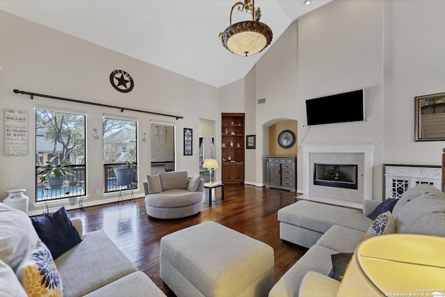 living room featuring baseboards, high vaulted ceiling, wood finished floors, and a tile fireplace