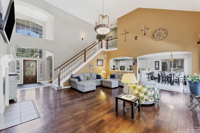 living area featuring arched walkways, high vaulted ceiling, stairs, and hardwood / wood-style flooring