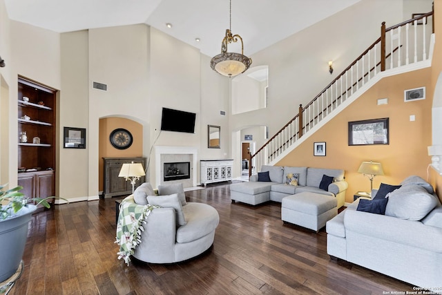 living area featuring stairs, visible vents, a glass covered fireplace, and dark wood finished floors