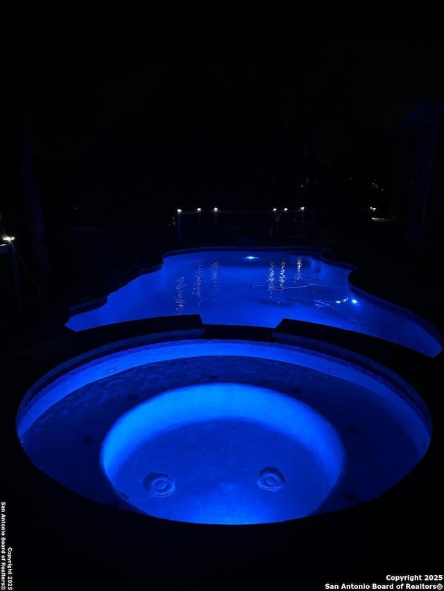 pool at night with an in ground hot tub