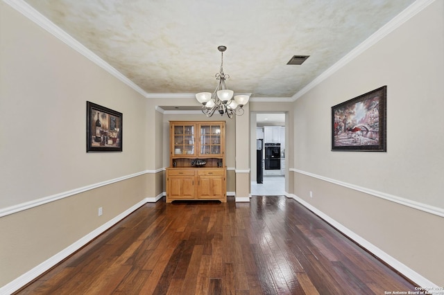 unfurnished dining area with baseboards, visible vents, dark wood finished floors, crown molding, and a chandelier