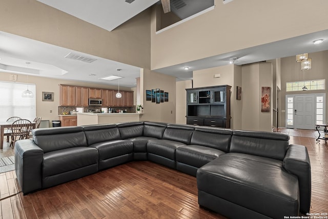 living room with dark wood finished floors, visible vents, a raised ceiling, and a high ceiling