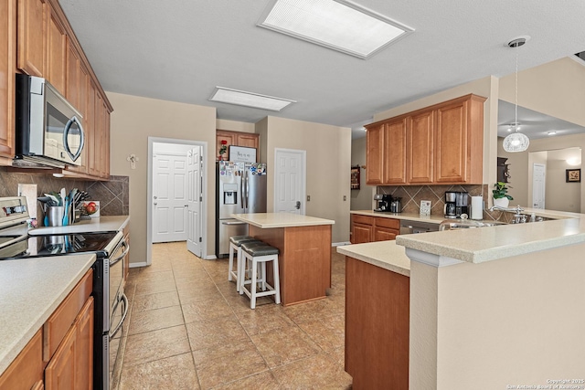 kitchen featuring a kitchen breakfast bar, backsplash, appliances with stainless steel finishes, a peninsula, and light countertops