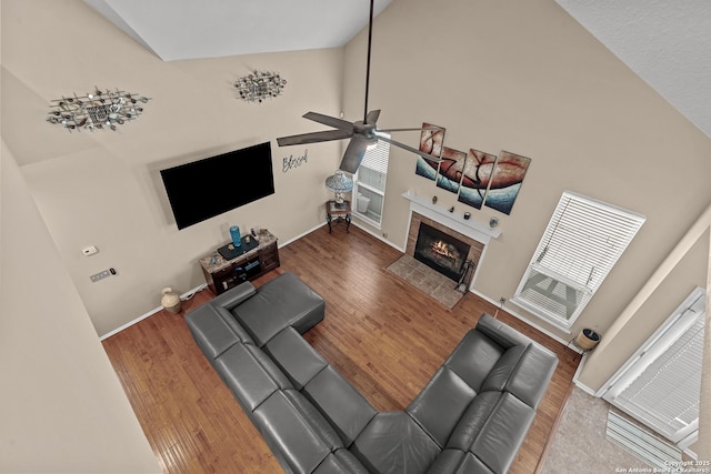 living room with baseboards, a tile fireplace, wood finished floors, high vaulted ceiling, and a ceiling fan