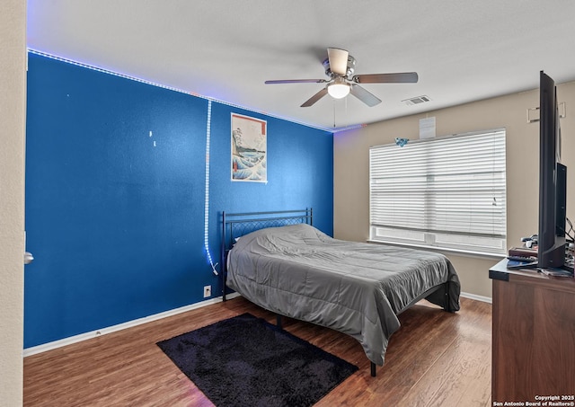 bedroom with a ceiling fan, wood finished floors, visible vents, and baseboards