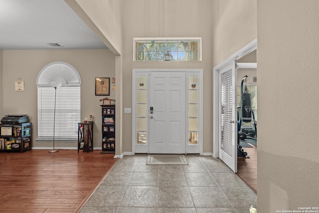 entrance foyer with visible vents, baseboards, a high ceiling, and wood finished floors