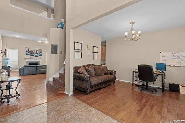 office space with wood finished floors, baseboards, an inviting chandelier, a fireplace, and a towering ceiling