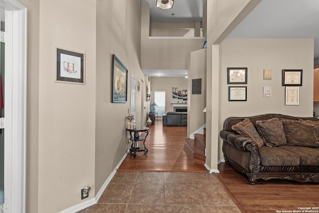 corridor with tile patterned flooring, a high ceiling, stairs, and baseboards