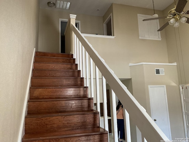 stairs featuring visible vents, ceiling fan, and a towering ceiling