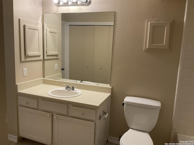 full bath featuring toilet, vanity, and a textured wall