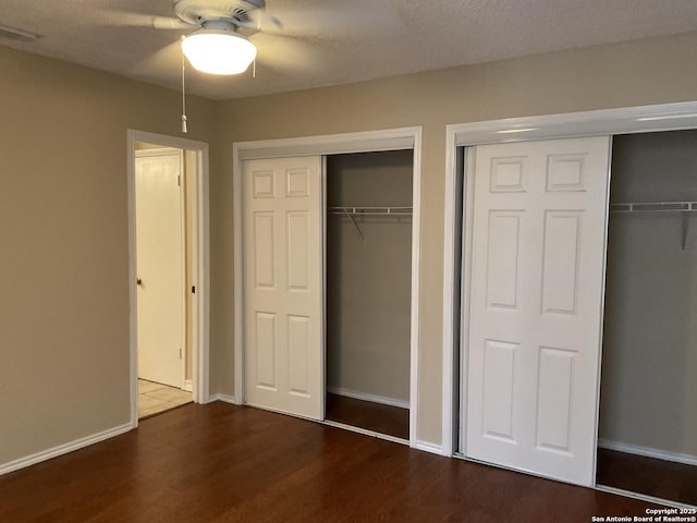 unfurnished bedroom with visible vents, multiple closets, baseboards, and dark wood finished floors