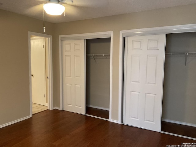 unfurnished bedroom featuring baseboards, a ceiling fan, multiple closets, and wood finished floors