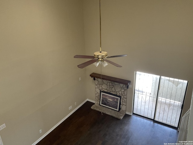 unfurnished living room featuring dark wood finished floors, a fireplace, baseboards, and a ceiling fan