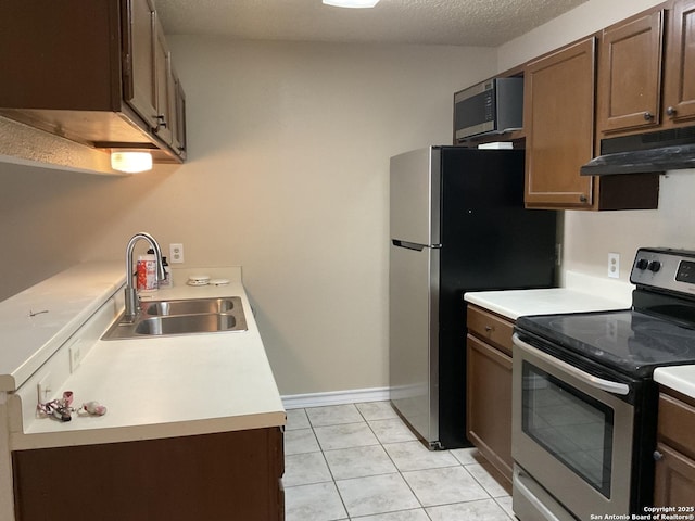 kitchen with a sink, light countertops, appliances with stainless steel finishes, a textured ceiling, and under cabinet range hood