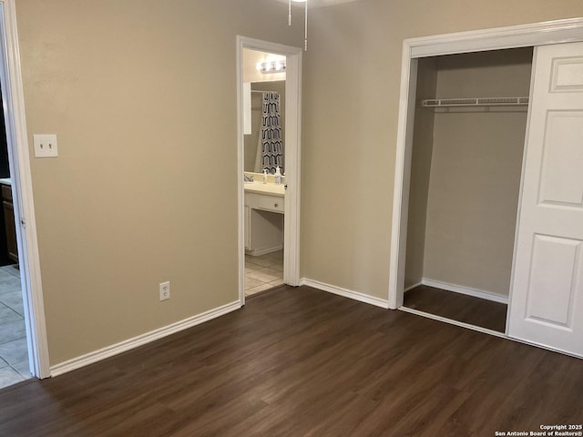 unfurnished bedroom featuring a closet, baseboards, ensuite bathroom, and dark wood-style flooring