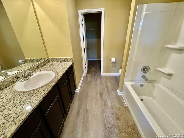 full bath with a spacious closet, baseboards, toilet, wood finished floors, and vanity