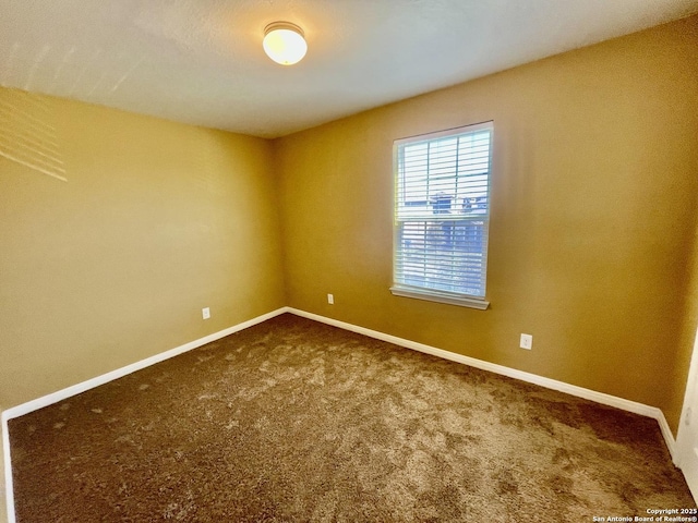 spare room featuring baseboards and dark colored carpet