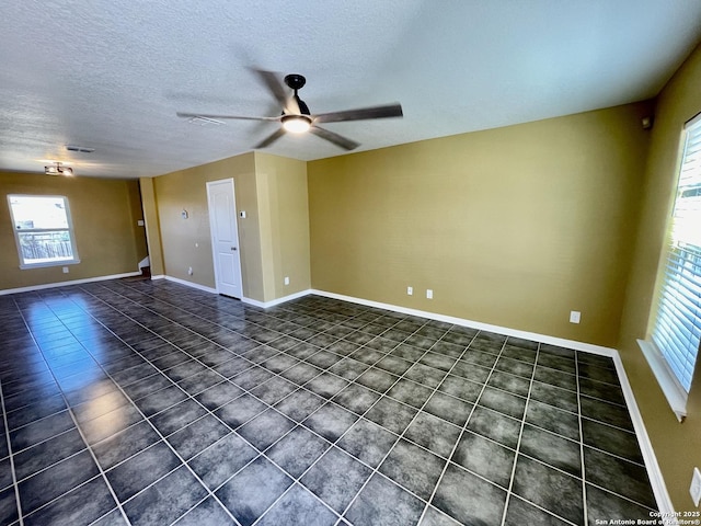 spare room with a textured ceiling, dark tile patterned flooring, baseboards, and ceiling fan