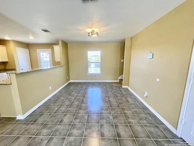 empty room featuring dark tile patterned floors, visible vents, baseboards, and a wealth of natural light