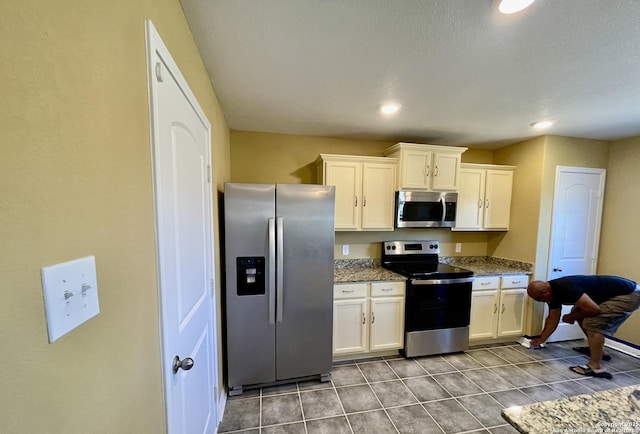 kitchen featuring tile patterned flooring, white cabinets, stone countertops, and appliances with stainless steel finishes