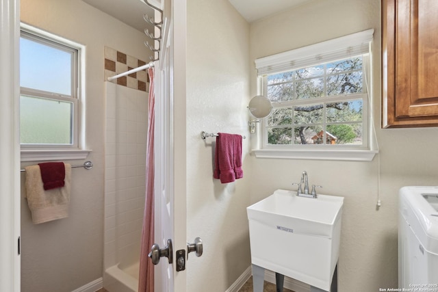 full bathroom featuring washer / clothes dryer, baseboards, a tile shower, and a sink