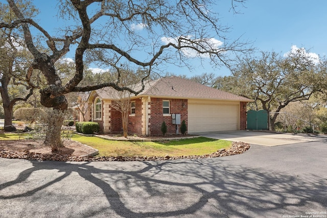 ranch-style home with a gate, concrete driveway, an attached garage, a shingled roof, and brick siding