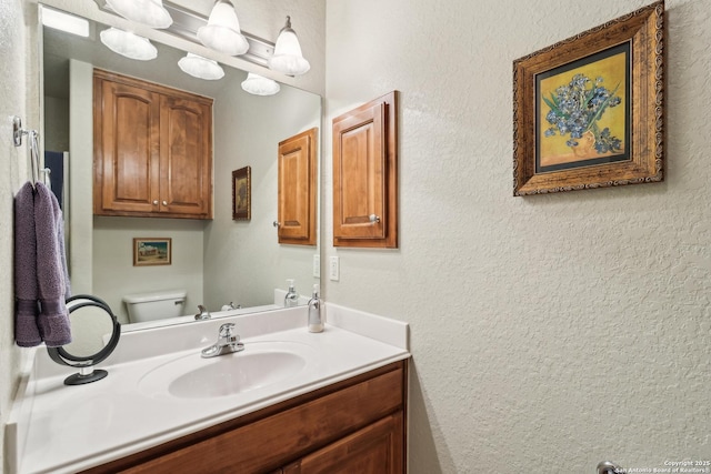 bathroom with vanity, toilet, and a textured wall