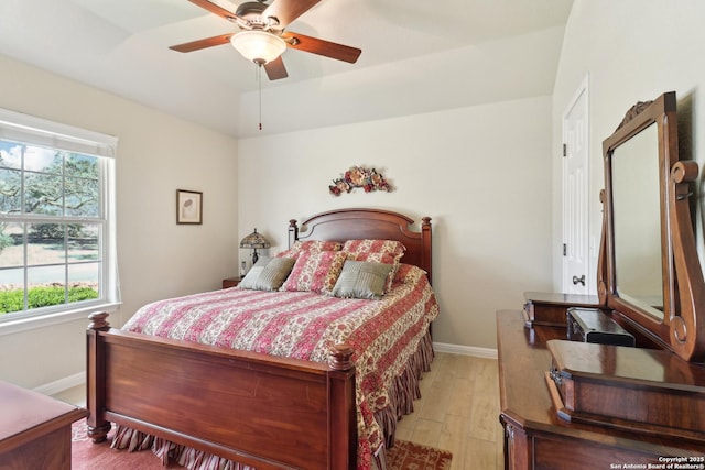 bedroom featuring a tray ceiling, baseboards, light wood finished floors, and ceiling fan