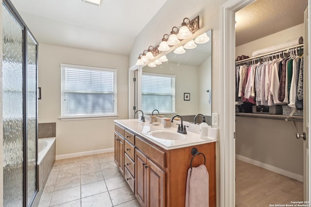 bathroom with a spacious closet, double vanity, vaulted ceiling, a bath, and a sink