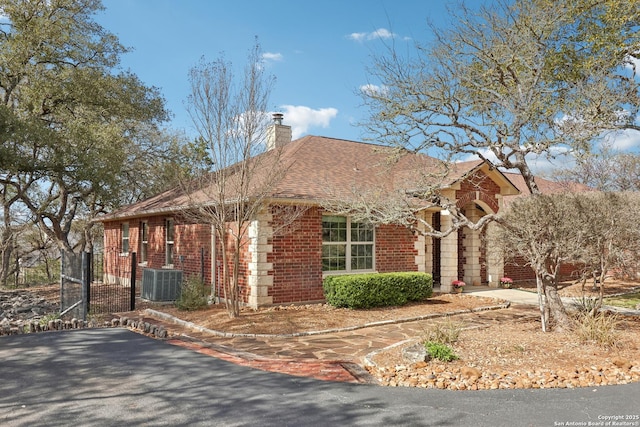 view of side of home with driveway, roof with shingles, a chimney, central air condition unit, and brick siding