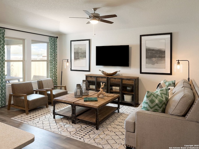 living room featuring a ceiling fan, light wood-style floors, baseboards, and a textured ceiling