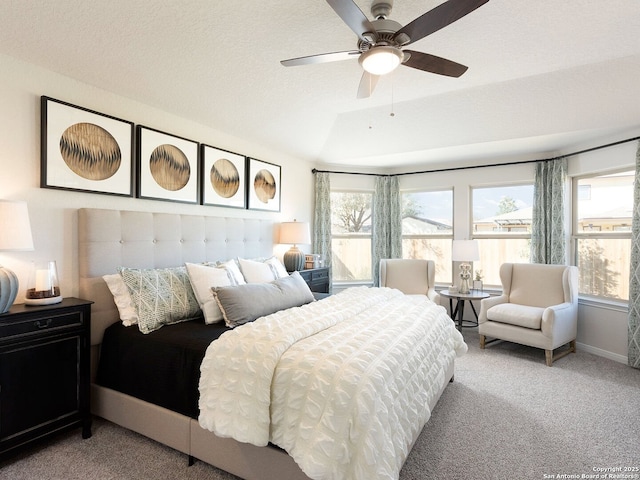 bedroom featuring a ceiling fan, baseboards, a textured ceiling, a raised ceiling, and light carpet