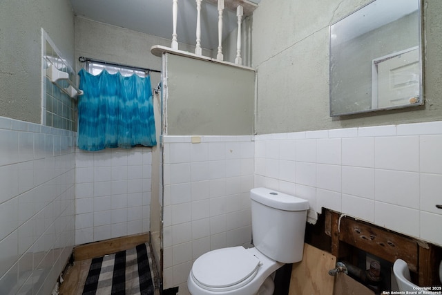 bathroom featuring a shower with shower curtain, wainscoting, tile walls, toilet, and a textured wall