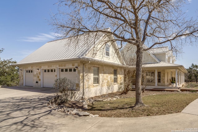 view of property exterior featuring metal roof, stone siding, covered porch, and concrete driveway