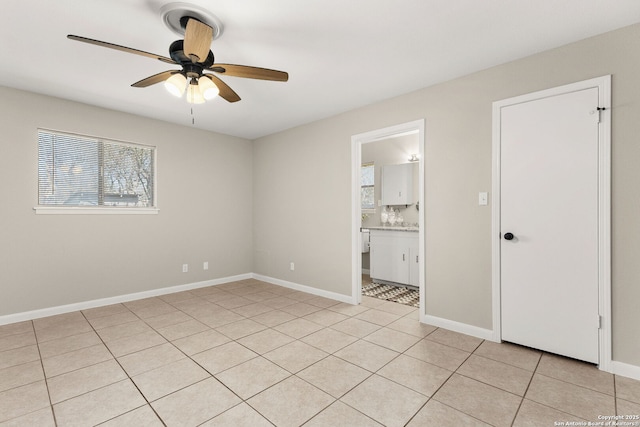 unfurnished bedroom with ensuite bathroom, baseboards, light tile patterned flooring, and a ceiling fan