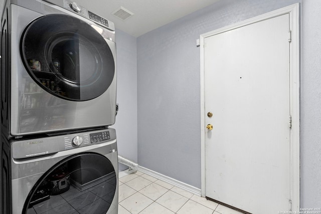 laundry area featuring stacked washer / dryer, visible vents, baseboards, light tile patterned floors, and laundry area