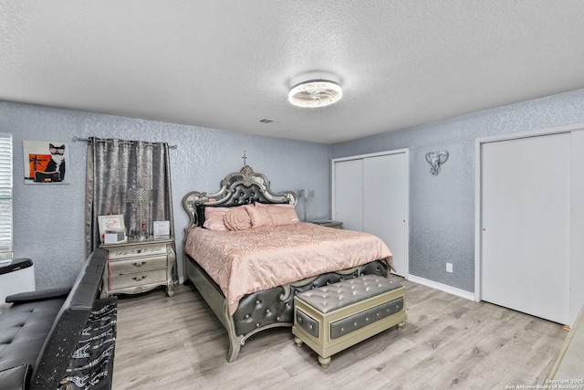 bedroom with multiple closets, a textured ceiling, wood finished floors, and a textured wall