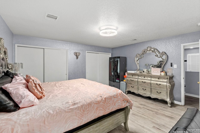 bedroom with visible vents, multiple closets, light wood-style flooring, a textured wall, and a textured ceiling