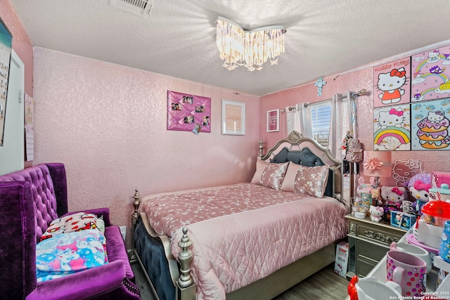 bedroom with visible vents, a notable chandelier, a textured ceiling, wood finished floors, and a textured wall