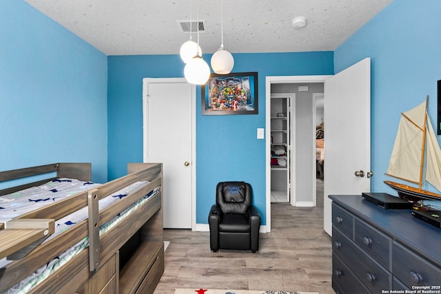 bedroom featuring visible vents, baseboards, a textured ceiling, and light wood finished floors