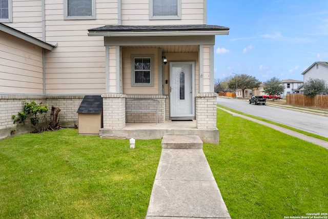 view of exterior entry featuring a yard, brick siding, and covered porch