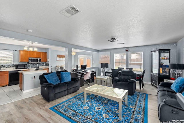 living room with light wood finished floors, visible vents, a wealth of natural light, and a textured ceiling