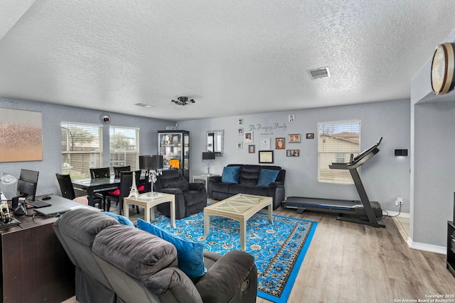 living area featuring visible vents, baseboards, a textured ceiling, and wood finished floors