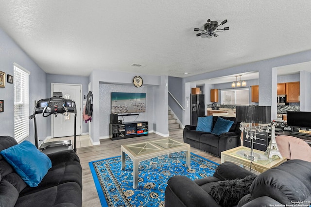 living room with light wood-type flooring, visible vents, a textured ceiling, baseboards, and stairs