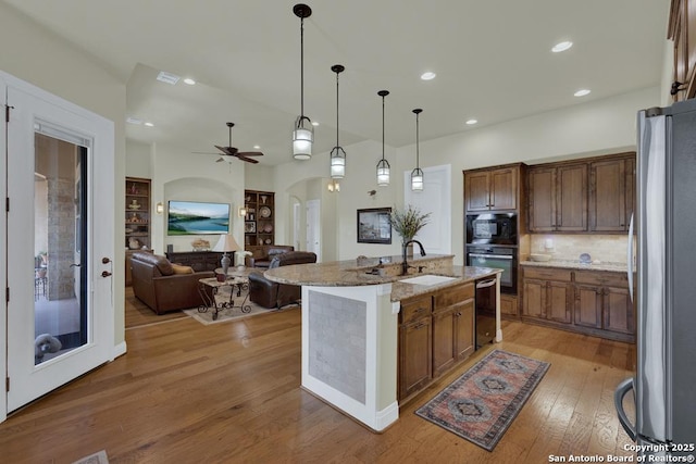 kitchen featuring light wood-type flooring, light stone counters, arched walkways, black appliances, and a sink