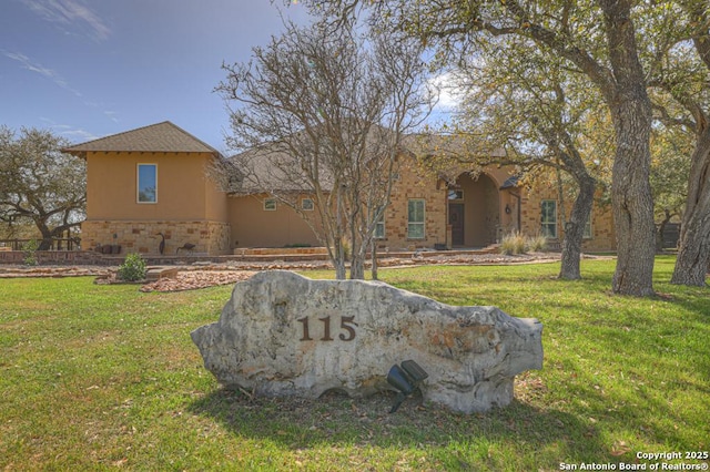 view of front facade featuring a front lawn, stone siding, and stucco siding