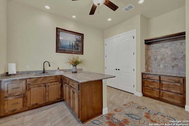 kitchen featuring visible vents, light stone countertops, brown cabinets, a peninsula, and a sink