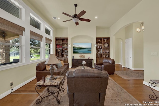 living room with built in shelves, arched walkways, and wood finished floors