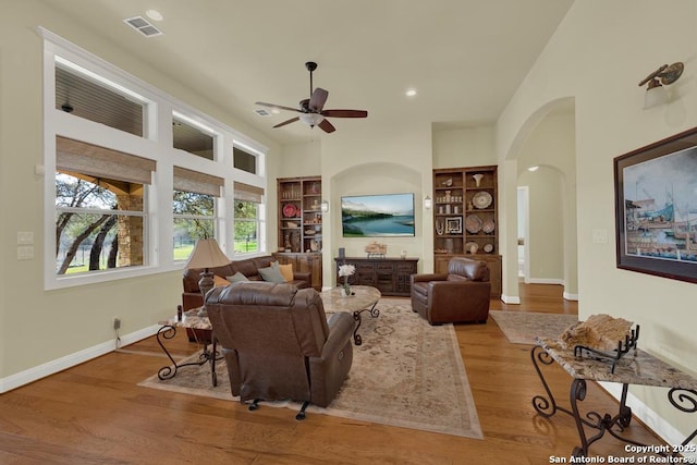 living area featuring visible vents, built in shelves, wood finished floors, arched walkways, and baseboards